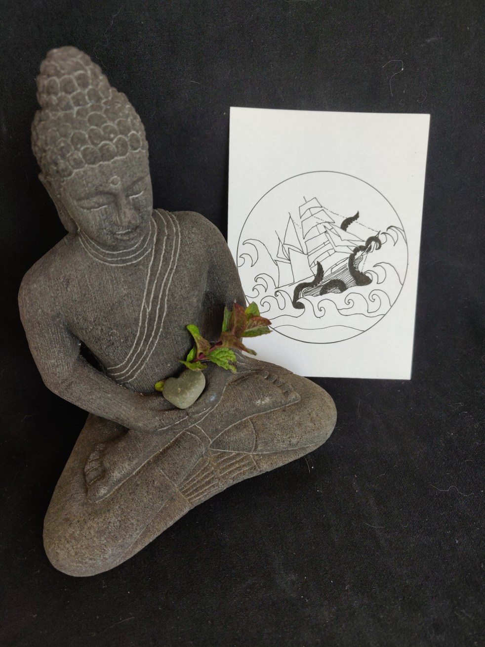 meditating statue with sprig of mint and drawing of a ship in rough waves and kraken tentacles grabbing the ship